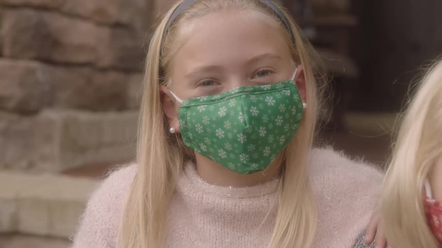 Blonde girl with a green mask faces the camera with eye contact