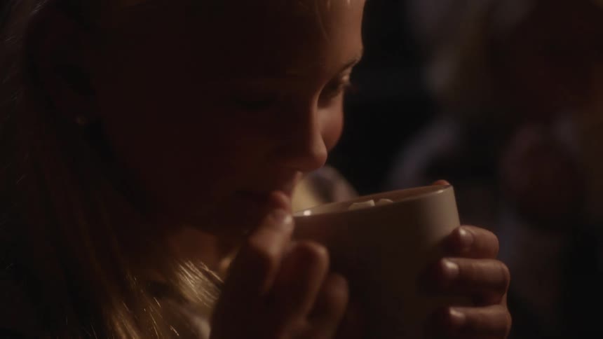 A girl smelling a cup of hot chocolate with marshmallows