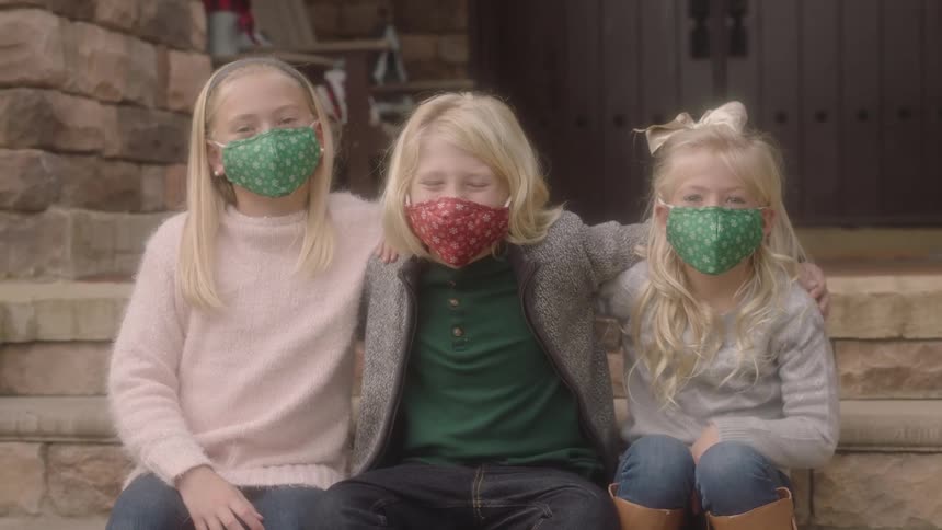 Three sisters with blue and red masks sitting on the stairs hold each other and looks at the camera