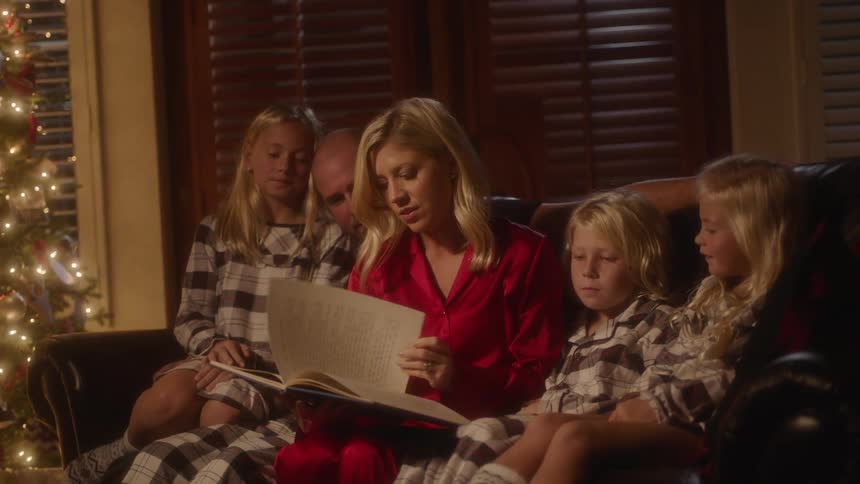 Children and adults gather on the couch as the woman reads a story