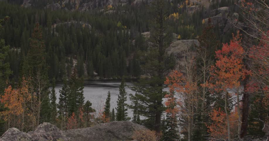 A lake sits in the distance between two hills covered with yellow and orange trees