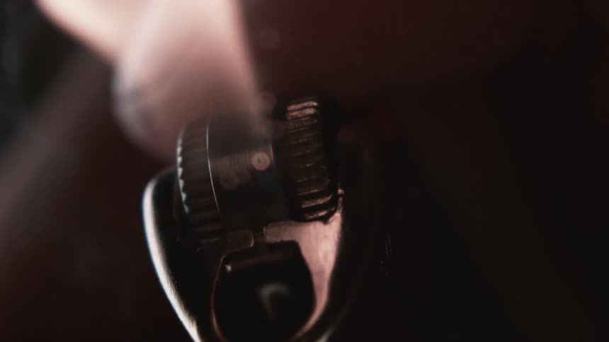 A finger pulls on a gear to strike a fire on a lighter