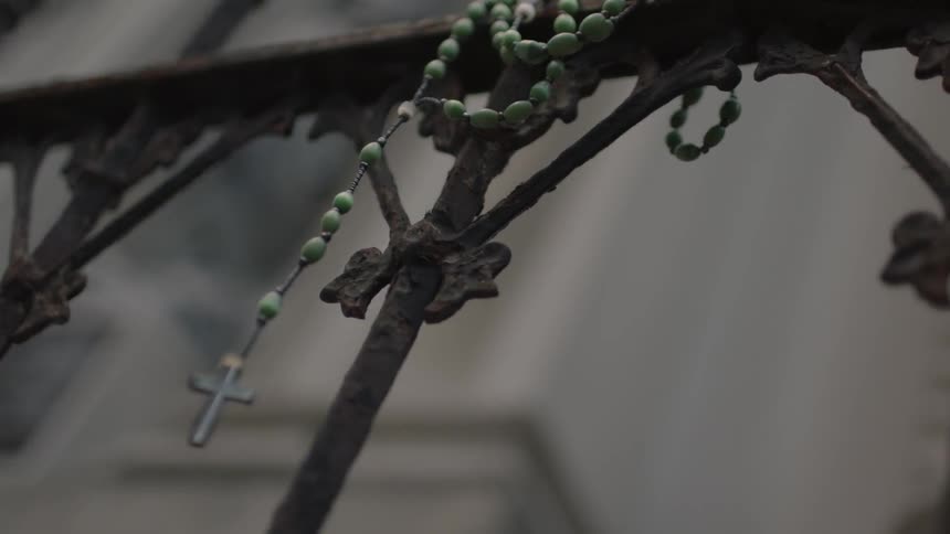 A cross on a necklace hanging from an iron gate
