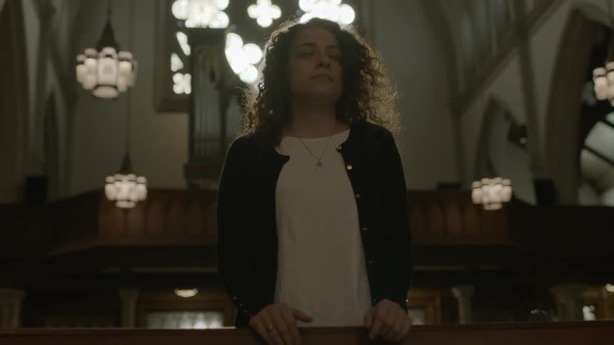 A woman walks up to a church pew and stands and looks forward
