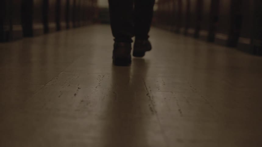 A man is walking down a long hall with wooden pews on each side