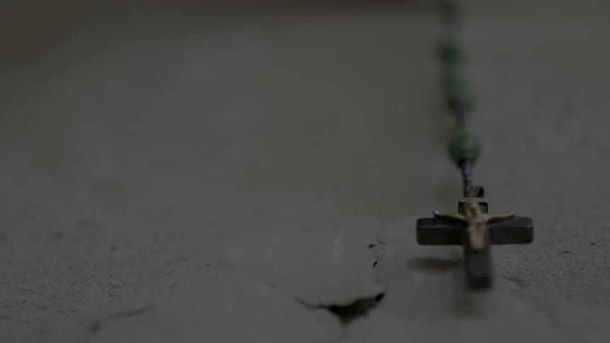 A cross on a rosary is hanging against a wall