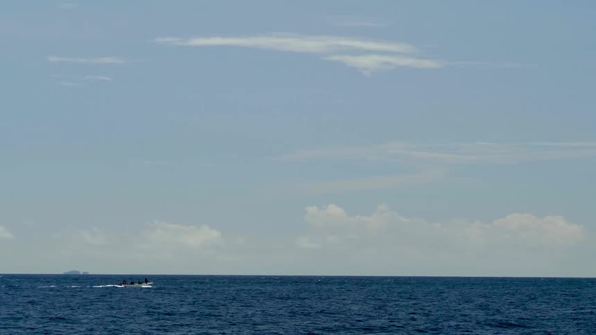 People travel in a boat across the open ocean under a clear daytime sky