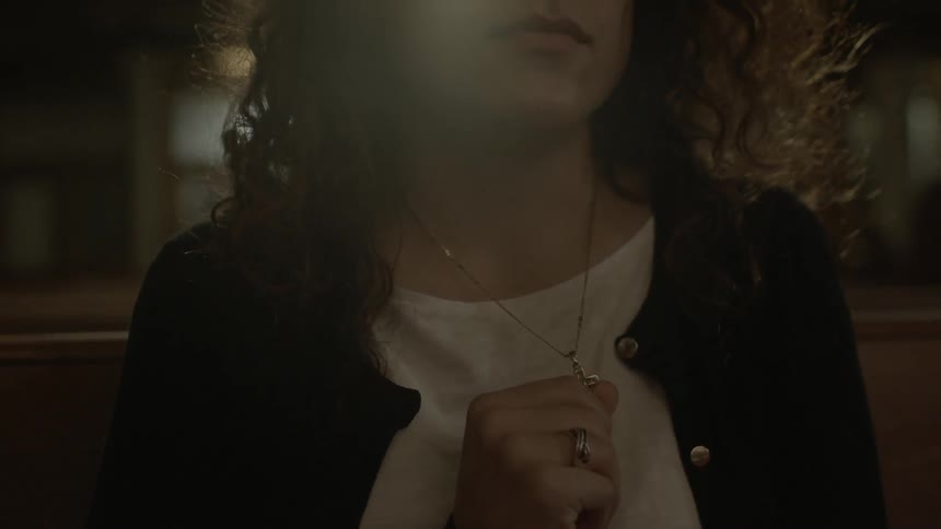 A woman grips her cross necklace while sitting on a church pew