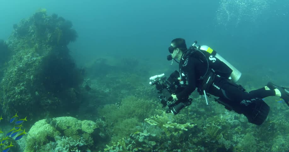 Scuba diver with camera equipment swimming near the rocky bottom of the hazy ocean waters