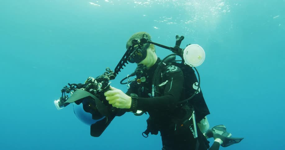 A male scuba diver is holding a camera under blue water