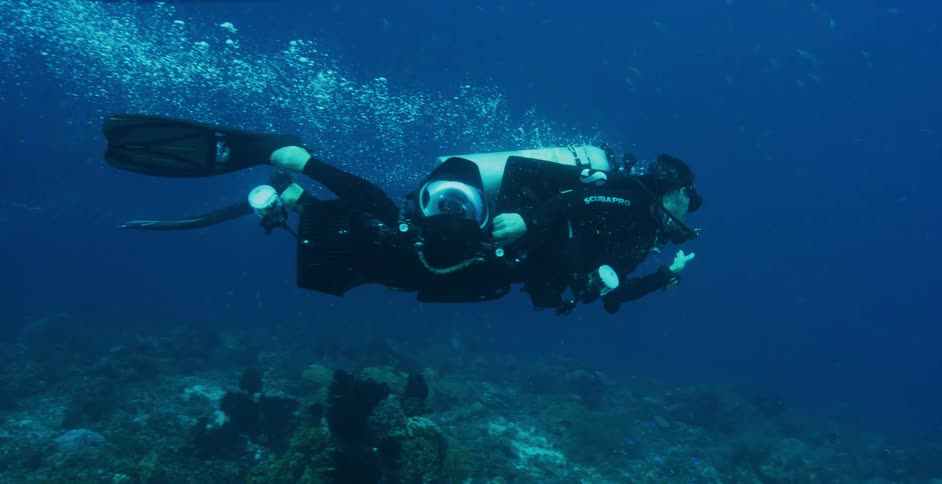 Man swims through water in scuba gear above a coral reef