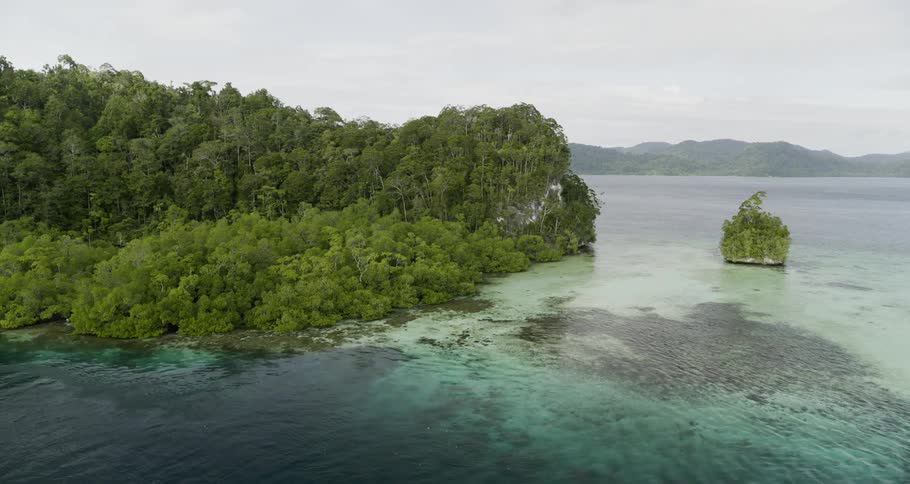 An aerial view of a lake with small islands and mountain ridges in the background on an overcast day