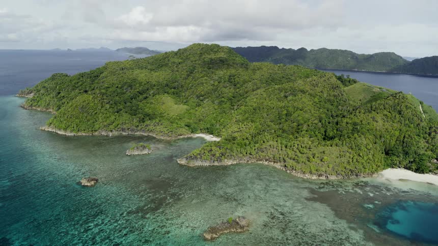 Island with lush vegetation against the ocean with islands in the background on a cloudy day
