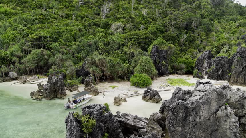 People on a boat landing on a beach with trees rocks the sky and clouds in the background