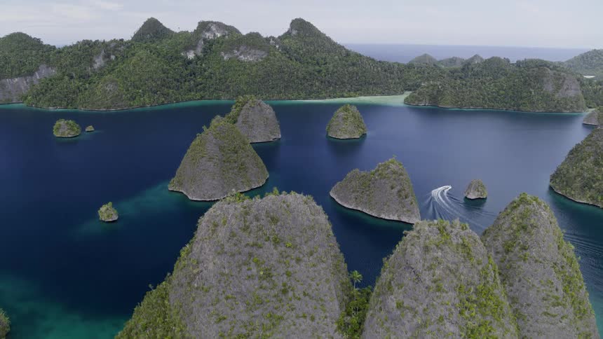 A speed leaves a trail in calm ocean waters as it navigates between small islands