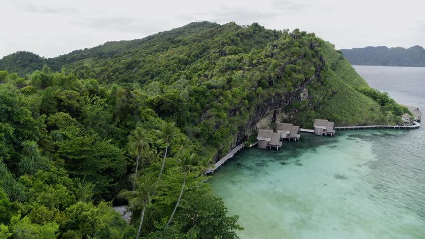 Huts on the coast of a large lush green island from a birds eye view