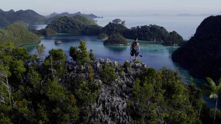 Man on top of a mountain surrounded by other mountains and bodies of water