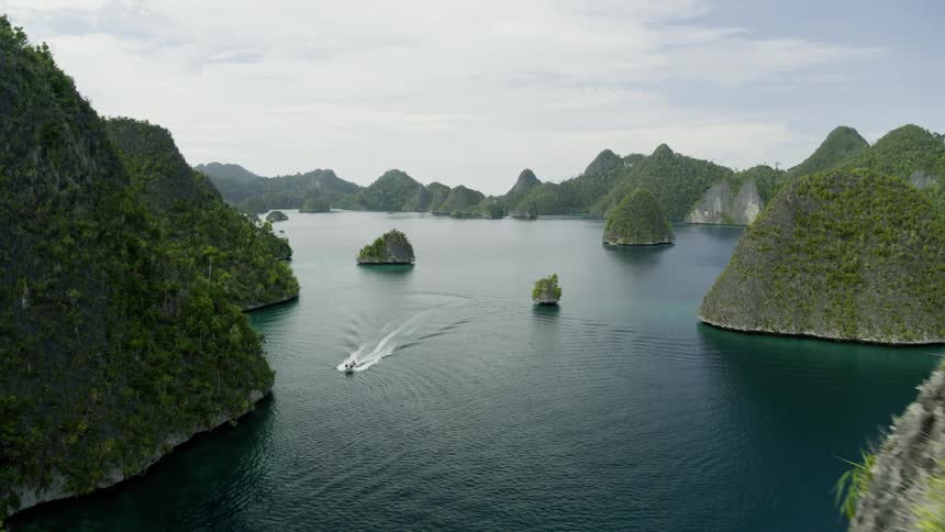 Large lush green islands and islets out at sea with a speedboat riding by