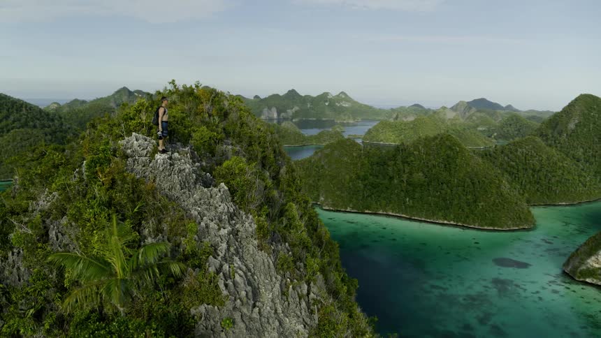 A person with a backpack and a camera standing on a cliff with the sky and clouds in the background