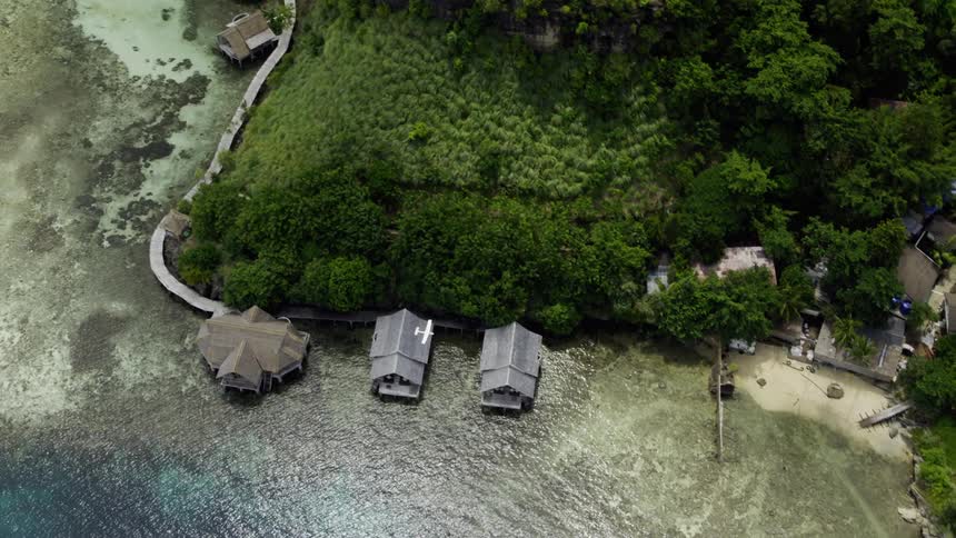 An island resort with houses near the coast with an airplane flying in the sky