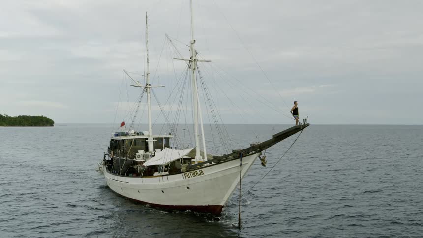 Man standing on the bow of a sailboat in the water while looking into the distance