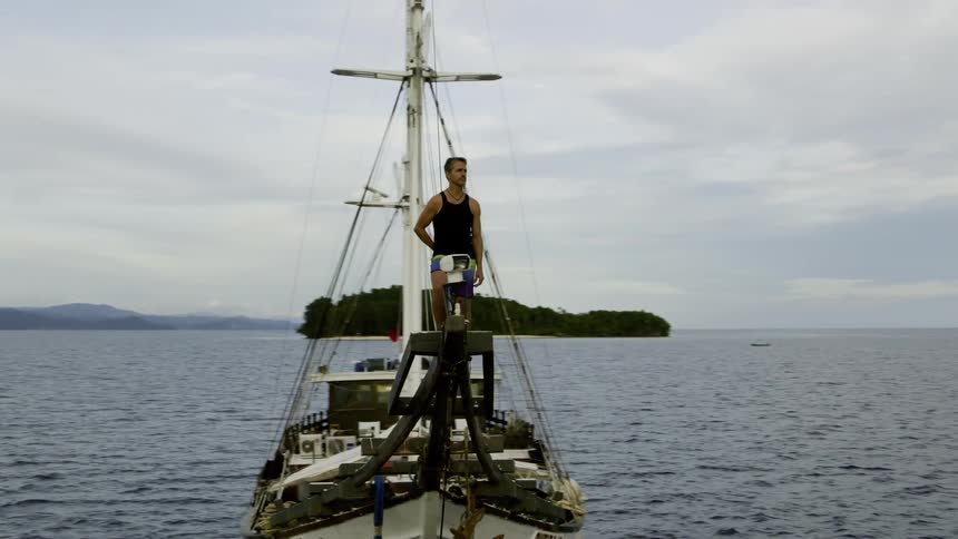 A man standing on a boat with the ocean land sky and clouds in the background