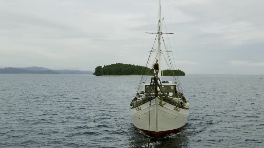 A man standing on the front of a boat as it sails through the ocean