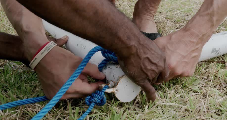 Two men try to tie two pipes together with a blue rope