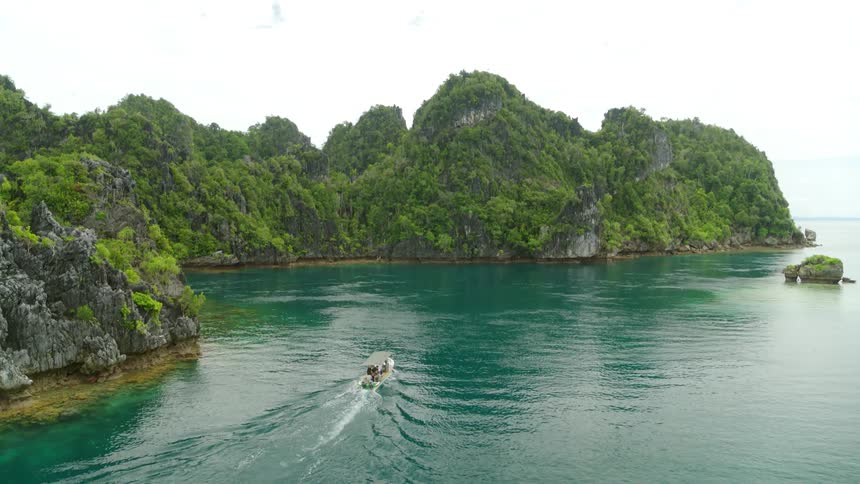 People ride a boat along the coast of a rocky landmass covered in vegetation