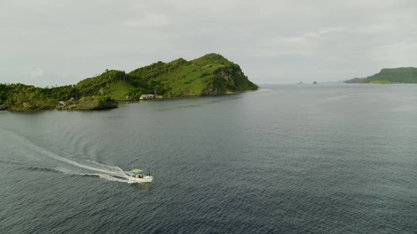 Boat sailing out at sea next to a coast of a tropical island