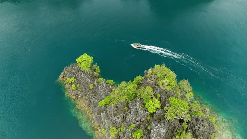 Boat riding out at sea surrounded by small mountains and islands in middle of the day