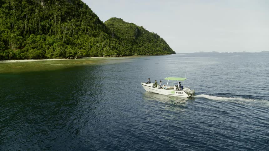 Boat with people onboard pulls up to a large island covered in trees and greenery