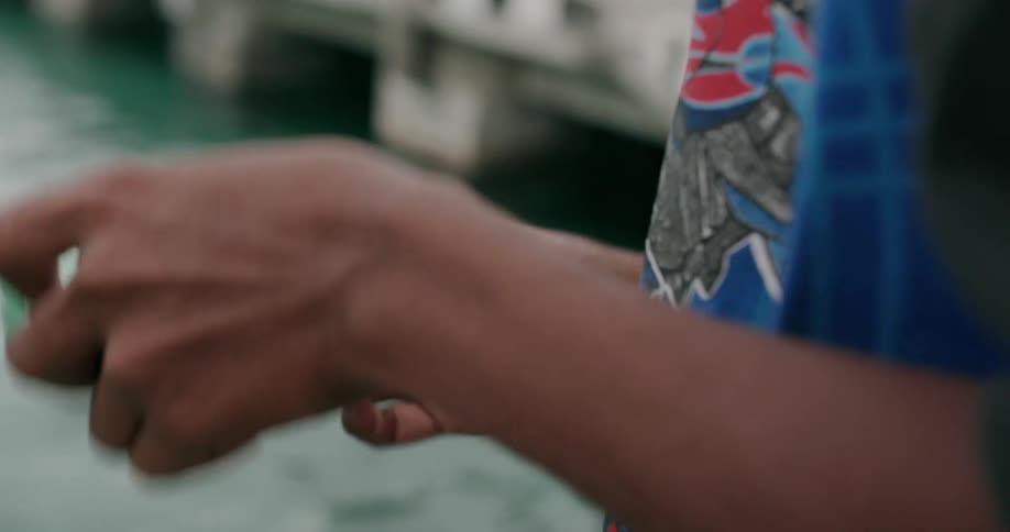 Boy wrapping a piece of string around a soda can next to a pier