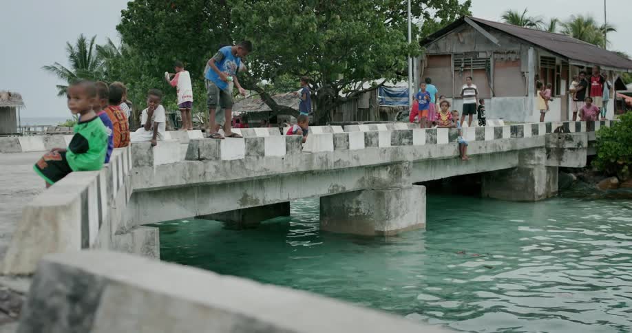 A group of young children hang out on a long waterside pier
