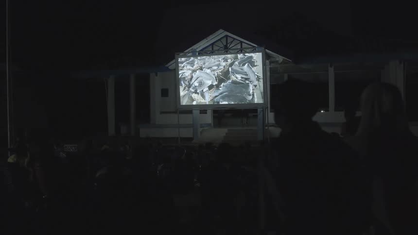 A large crowd watches a projected film outdoors
