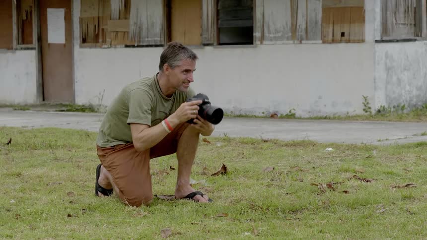 Middle aged white man kneels on the grass laughs and takes a picture