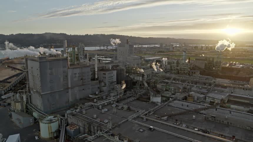 Tilt up reveal of a enormous factory facility set amidst a vast industrial landscape as the sun sets in the distance