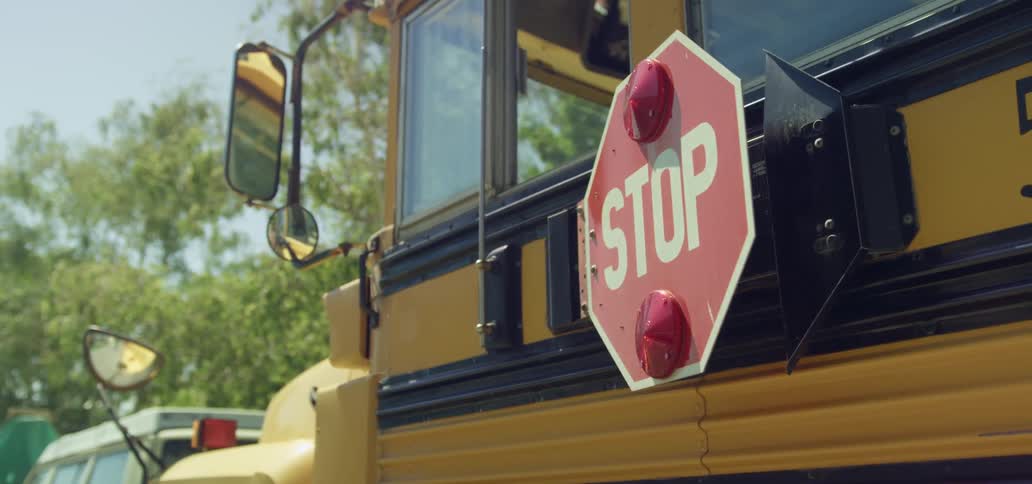 A school bus with a stop sign retracting with trees the sky and clouds in the background
