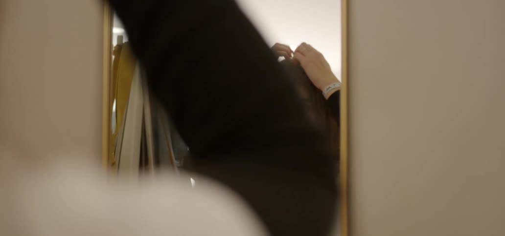 A young woman is running her hands through her hair as she looks into a mirror on the wall