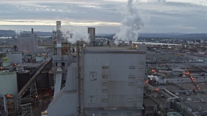 Orbiting around a filthy factory building as pollution pours out of multiple smoke stacks