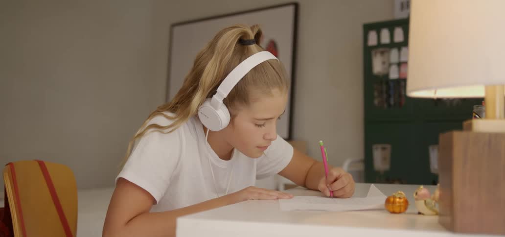 A teenager listens to music while doing homework in her room