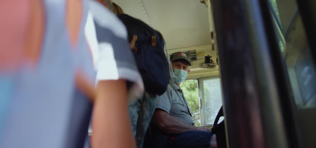 A man with a hat and a mask opening a school bus and letting children in