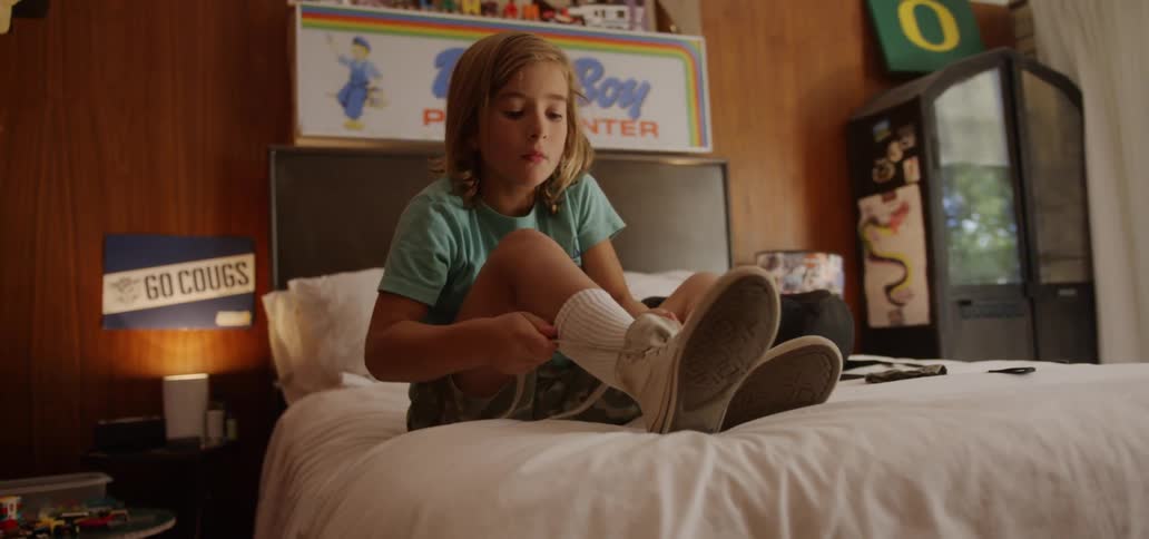 A boy ties his shoes while sitting on his bed in his bedroom during the day