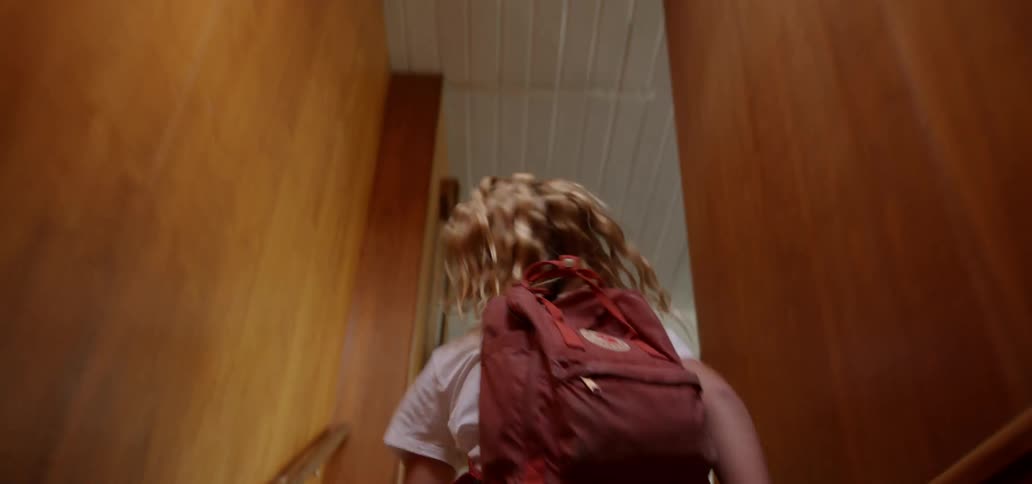 A teenage girl runs up the stairs to the front door in her house