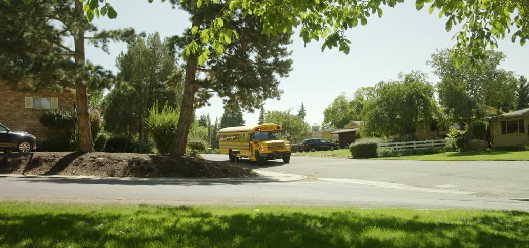 A school bus is coming to a stop on a corner of a street in a neighborhood during the day