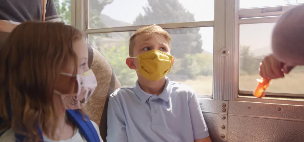 A boy is sitting on a school bus with other kids shaking his head