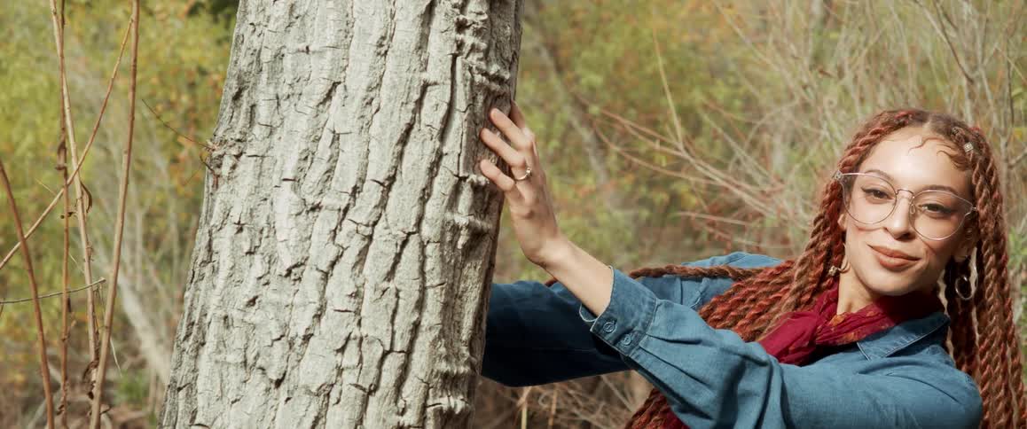 A woman is standing outdoors by a tree