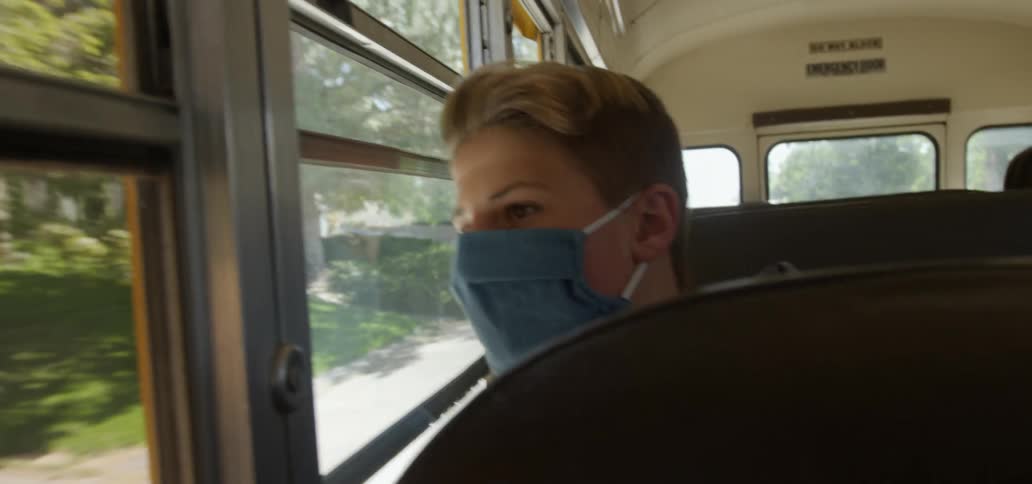 A boy sits in a school bus looking out the window as it drives through a neighborhood