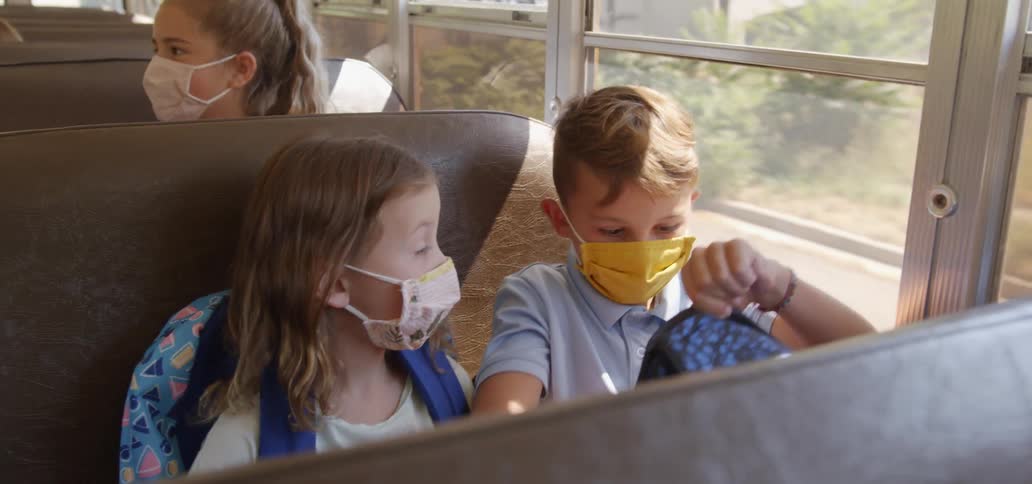 A young boy and girl sit together on a school bus looking in the boys back pack