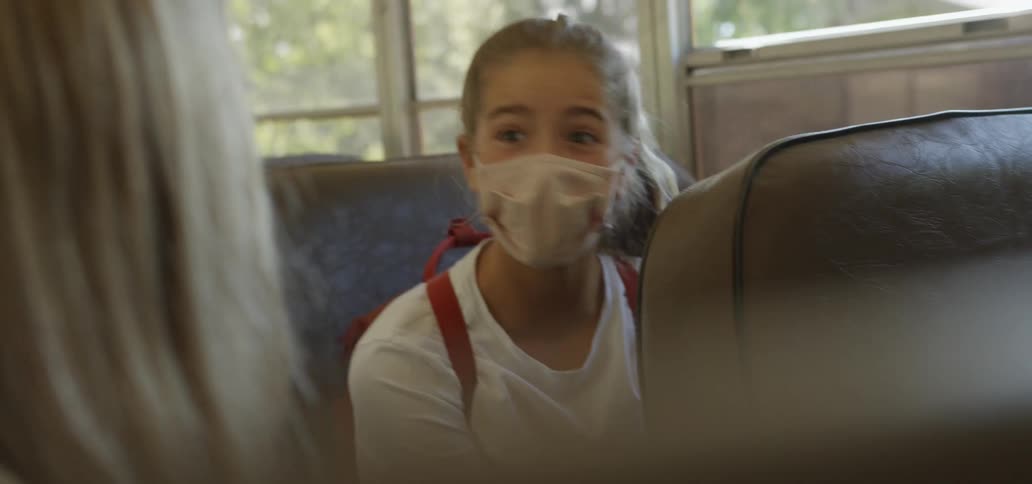 Teenager with a mask on sitting on a bus talking to her friend